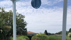 Een terras bij het zwembad met uitzicht op het zwembad, omgeven door groen en een huis op de achtergrond.