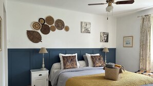 Een slaapkamer met een bed, nachtkastjes, een plafondventilator, wanddecoratie en een raam met gordijnen.