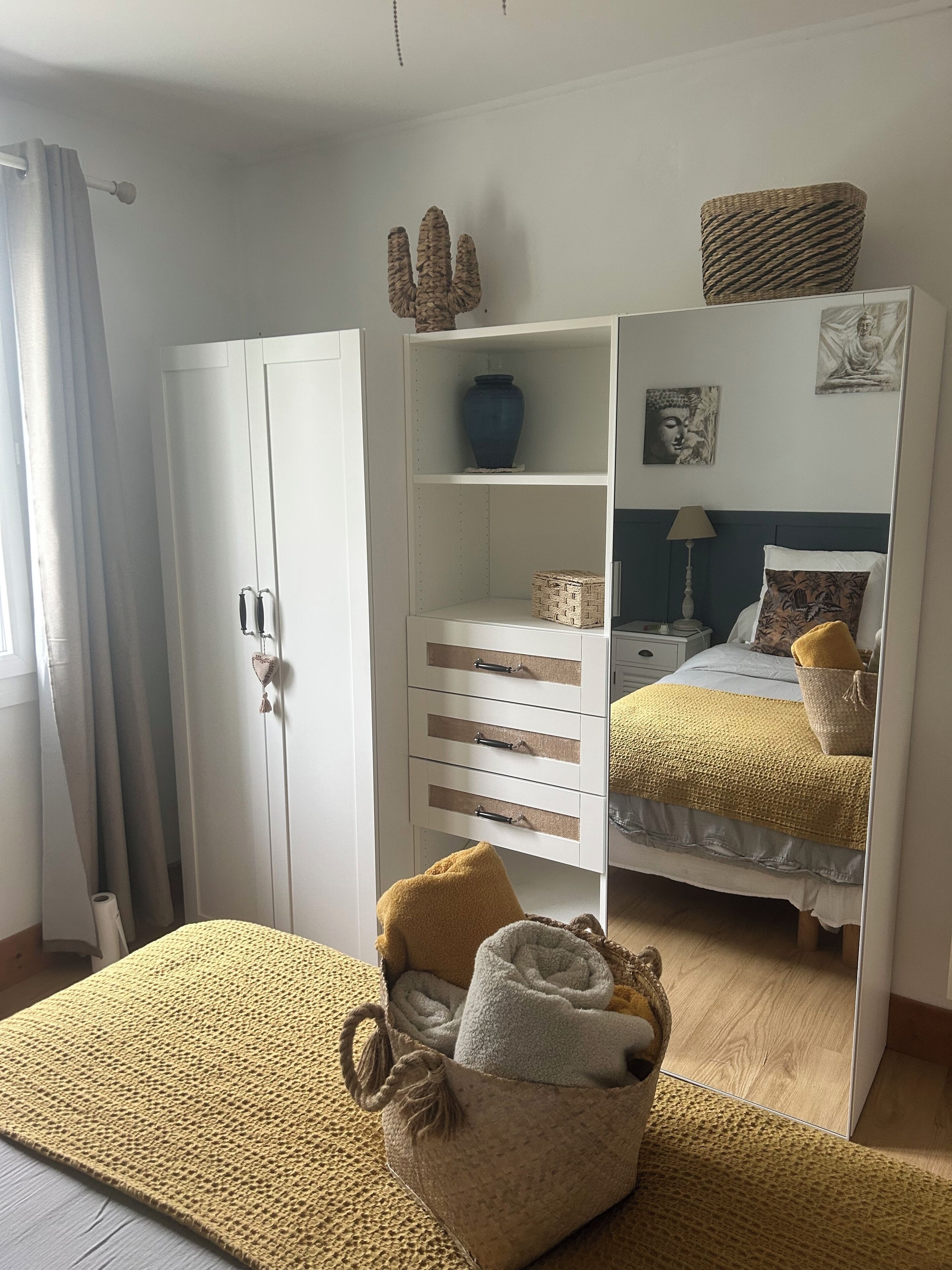 A bedroom with a bed, a wardrobe, a mirror, and a small seating area with cushions.