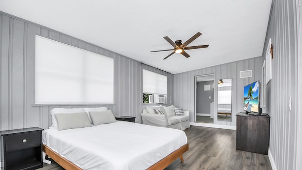 Une chambre avec un grand lit, un ventilateur de plafond, une télévision et une vue sur l’extérieur.