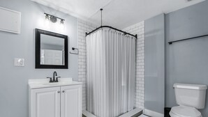 Une salle de bain avec un lavabo blanc, un miroir, un rideau de douche et des toilettes.