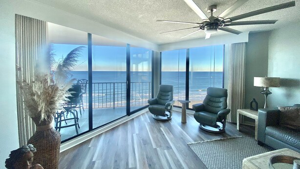 A spacious room with a large balcony overlooking the ocean, featuring two reclining chairs and a ceiling fan. - Direct Luxury Ocean Front 
Includes umbrella - 2 chairs set up daily 5/31-9/5 (Murrells Inlet)