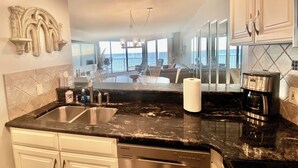 A kitchen with a black marble countertop, stainless steel appliances, and a view of the ocean through large windows. - Direct Luxury Ocean Front 
Includes umbrella - 2 chairs set up daily 5/31-9/5 (Murrells Inlet)