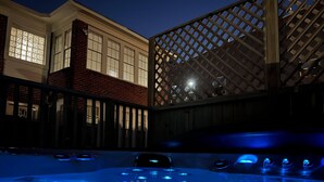 A hot tub with blue lighting, a brick building, and a wooden lattice structure in the background.