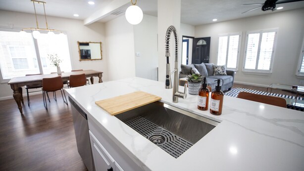 A modern kitchen with a white marble countertop, a built-in sink, and a wooden cutting board. There are two bottles of hand soap on the countertop.