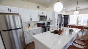 A modern kitchen with white cabinets, stainless steel appliances, a marble island, and brown leather bar stools.