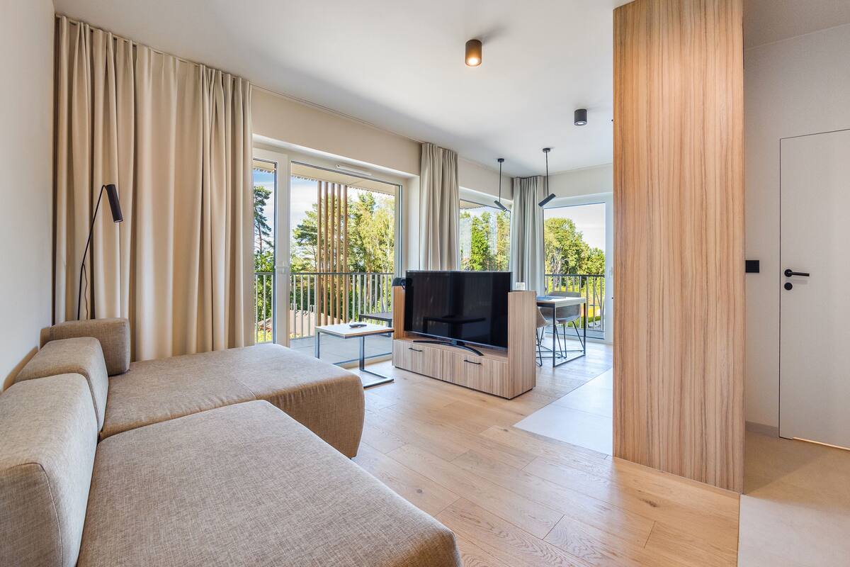 A modern living room with a sofa, a flat-screen TV, and a balcony with a table and chairs.