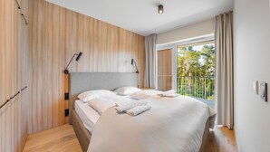 Une chambre moderne avec un grand lit, un mur d’accent en bois, une vue sur les arbres depuis un balcon et un luminaire au plafond.