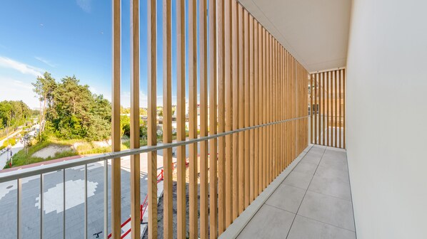 A balcony with wooden slats, a metal railing, and a view of a road and greenery. - Sun & Snow Bałtycki Apartamenty (Swinoujscie)
