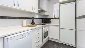 Una cocina moderna con armarios blancos, microondas integrado, horno y lavavajillas.