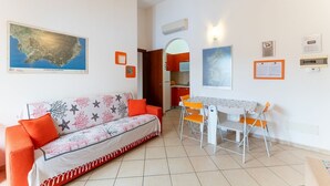 A living room with a sofa, dining table, chairs, and a map on the wall. - Orange House, 5 minutes from Chia (Domus De Maria)