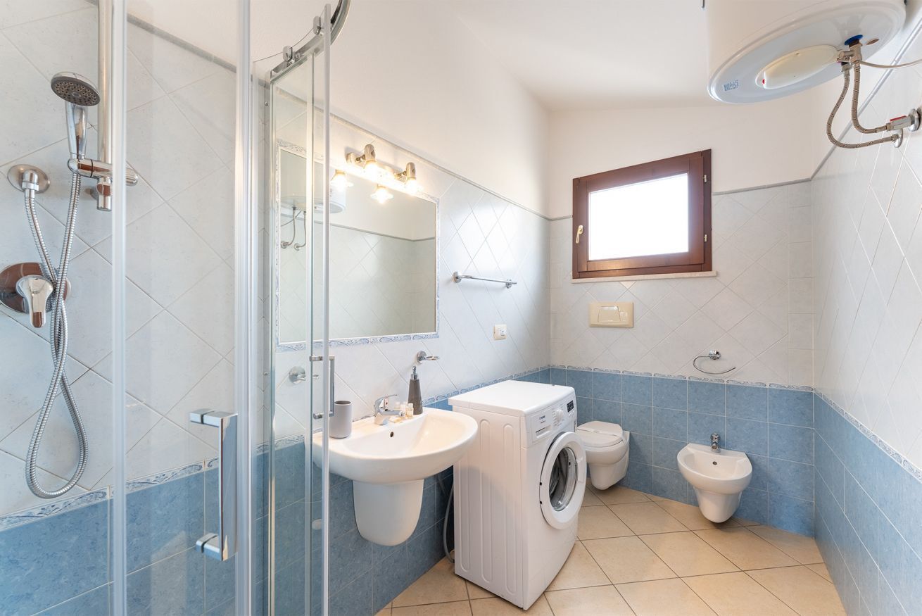 Ein Badezimmer mit Glasdusche, Waschbecken, Waschmaschine und Duschtoilette.