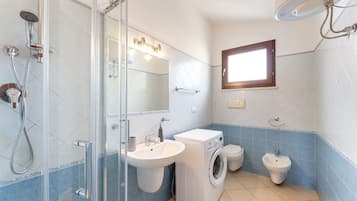 Ein Badezimmer mit Glasdusche, Waschbecken, Waschmaschine und Duschtoilette.