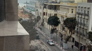 Une vue d’une rue de la ville, avec des immeubles, une route et une plage au loin.