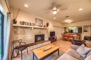 A living room with a stone fireplace, a sofa, a coffee table, and a bookshelf. - CW C109 River Bend (New Braunfels)