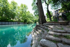 A tranquil outdoor area with a clear water body, stone steps, and a metal railing. - CW C109 River Bend (New Braunfels)