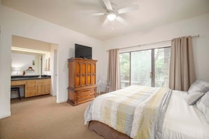 Une chambre à coucher comprenant un lit, un ventilateur de plafond, une fenêtre avec des rideaux, une armoire en bois et un téléviseur.