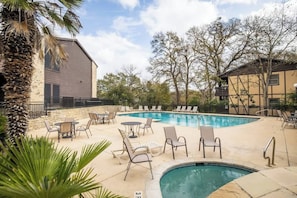 Un espace piscine doté de chaises longues et de tables, entouré d’immeubles et d’arbres.