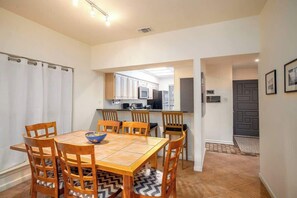 A dining area with a wooden table and chairs, a kitchen in the background, and a door leading to another room. - CW C109 River Bend (New Braunfels)