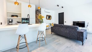 A modern kitchen with a white countertop, two bar stools, a dark sofa, and pendant lighting. - Blue Bay | The Reef | Terrace (Sint Michiel)