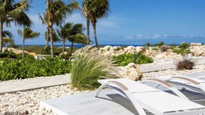 A beachside lounge area with white lounge chairs, palm trees, and a view of the ocean. - Blue Bay | The Reef | Terrace (Sint Michiel)