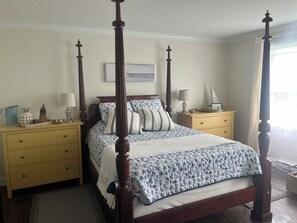 Cozy four-poster bed sits centrally in a serene room with cream-colored walls, complemented by a nightstand and lamp on each side.