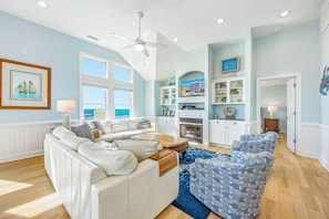 A spacious living room with a white sofa, blue patterned chair, and a fireplace. - Premier Oceanfront Dog Friendly w/ Pool, Elevator, Hot Tub, Game Rm, Outdoor Bar (Hatteras)