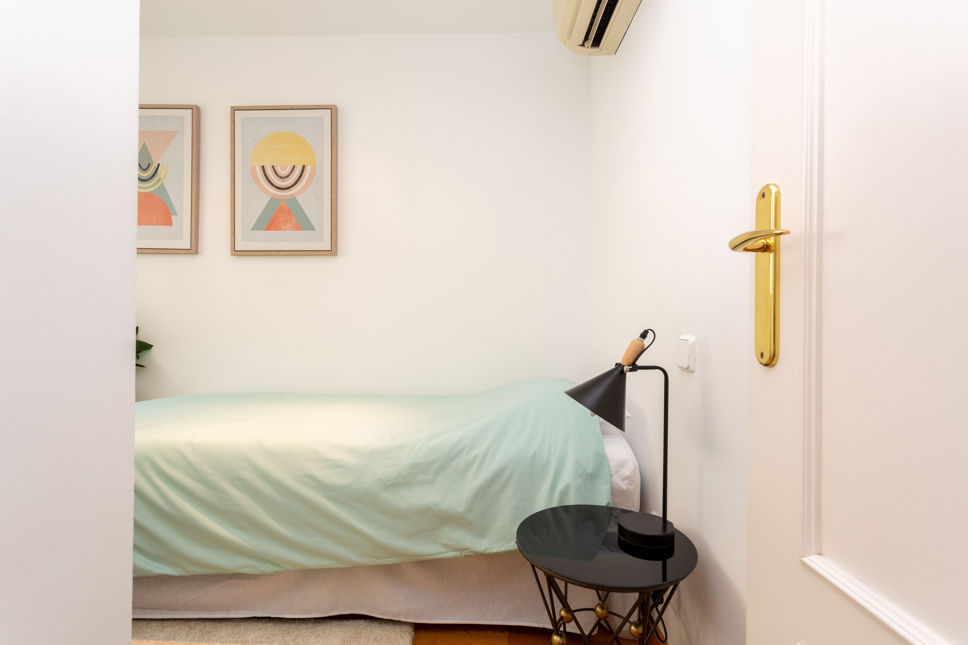 Una camera da letto piccola e ordinata con un letto singolo, un comodino e due opere d'arte incorniciate appese al muro.