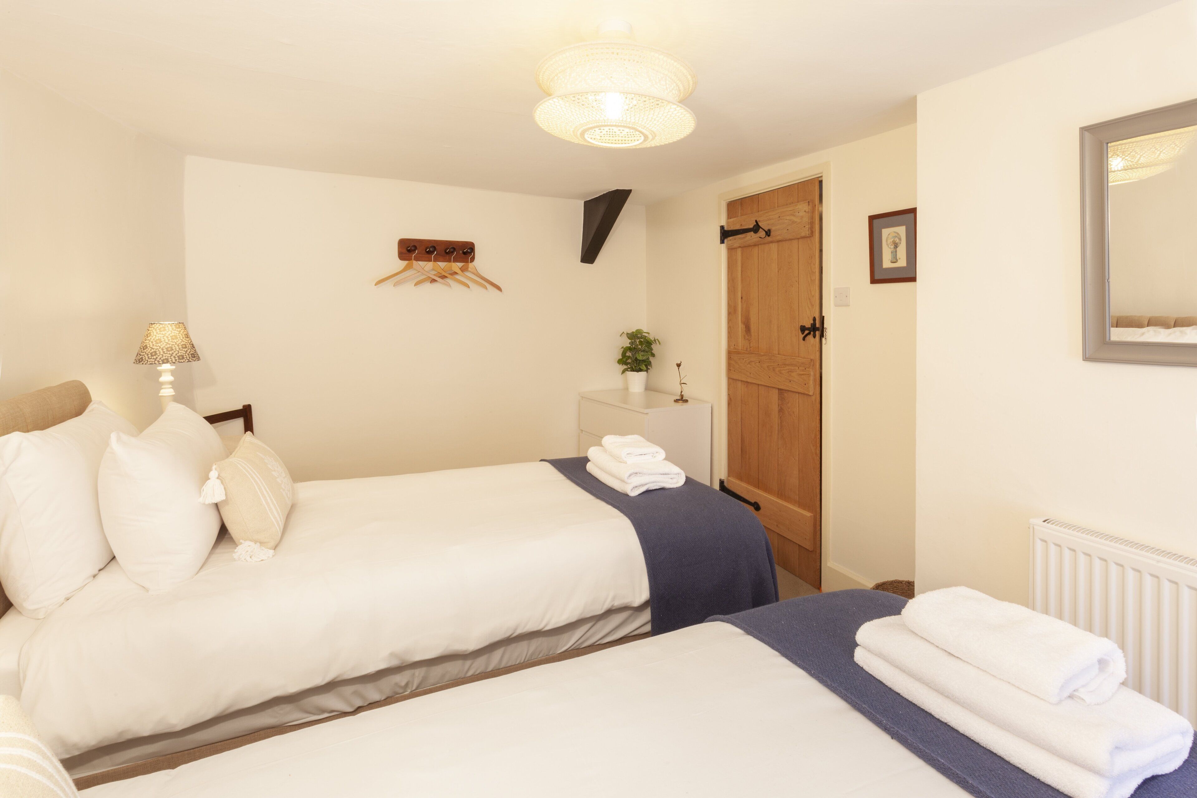 Een hotelkamer met twee bedden, een houten deur, een witte radiator en een spiegel aan de muur.