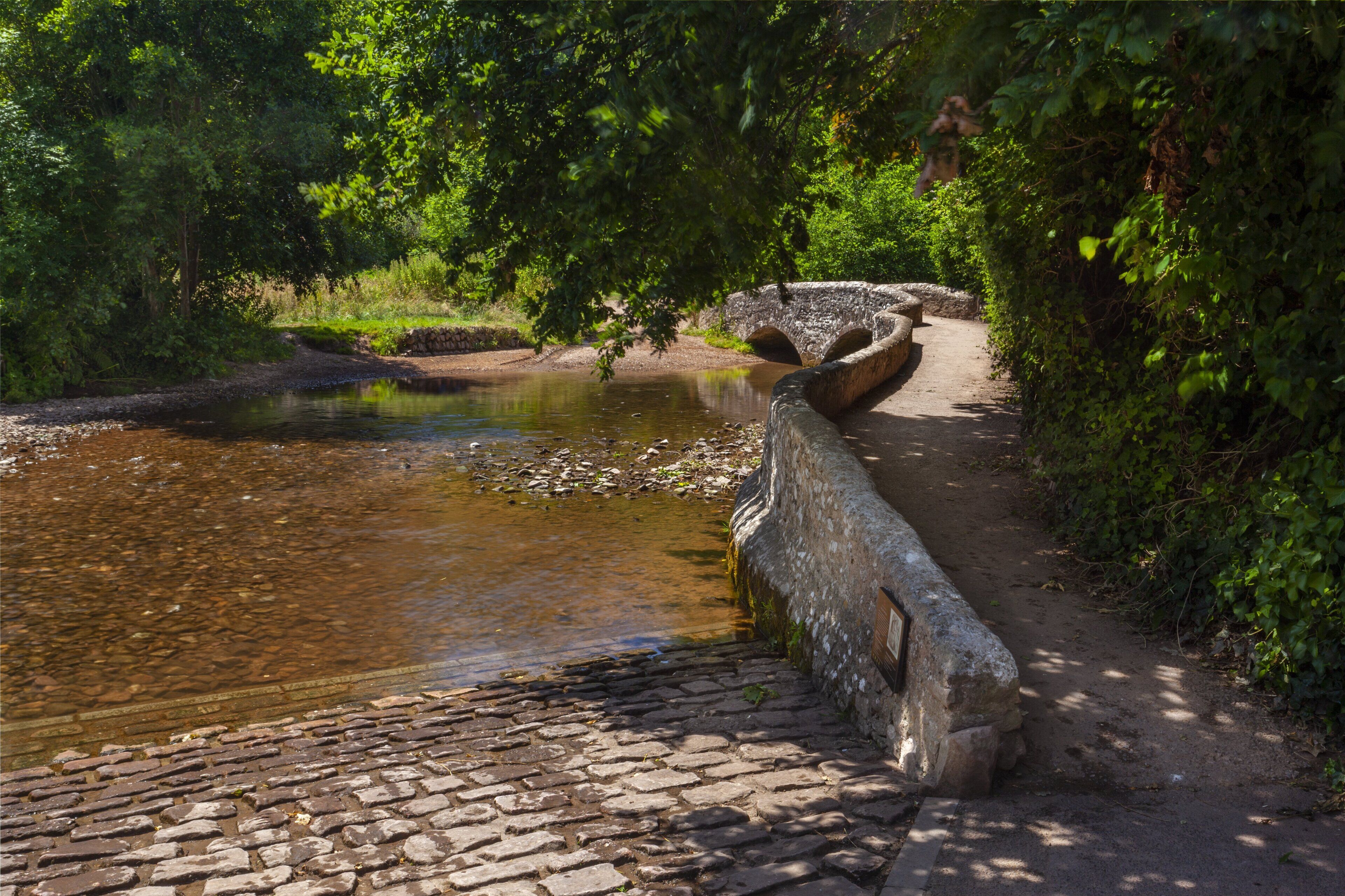 Eine steinerne Brücke über einem ruhigen Fluss, umgeben von üppigem Grün.