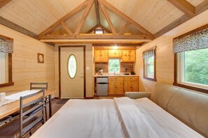 Quarto de cabana de tronco com uma cama, uma escrivaninha e um pequeno espaço de cozinha.