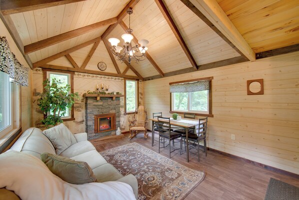 A cozy cabin interior with a fireplace, wooden walls, a dining area, and a large window.