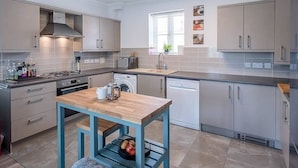 A modern kitchen with grey cabinets, a wooden table, and a washing machine. - 53 Bibby's Way, Framlingham (Woodbridge)