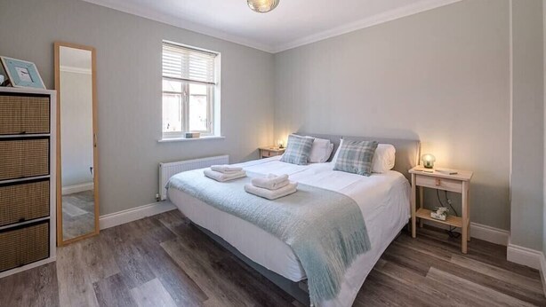 A bedroom with a large bed, bedside tables, a mirror, and a window. - 53 Bibby's Way, Framlingham (Woodbridge)