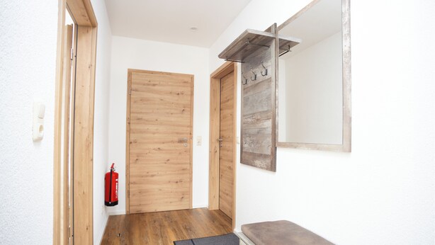 Un pasillo con puertas de madera, un extintor, un banco y un espejo en la pared.