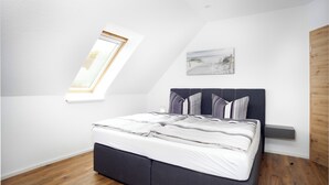 Un dormitorio con cama, tragaluz, un cuadro y suelo de madera.