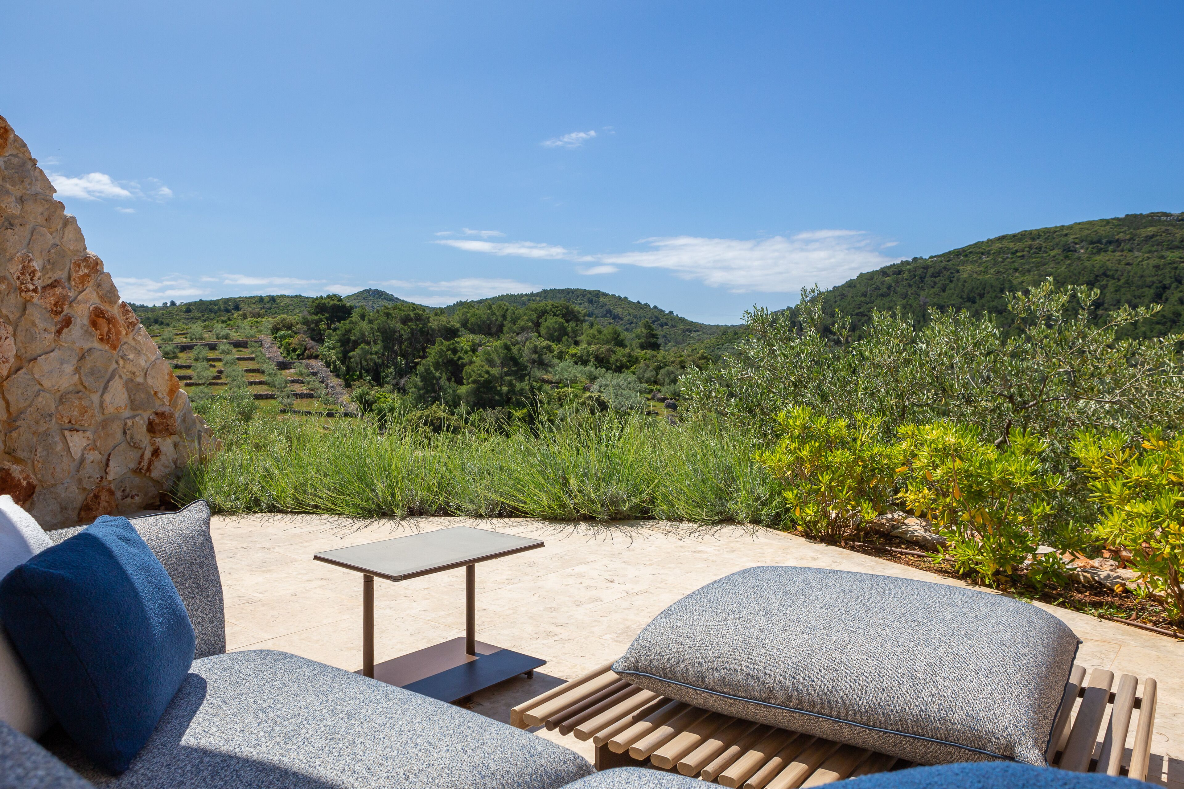 An outdoor seating area with a stone wall, a table, and a view of green hills.