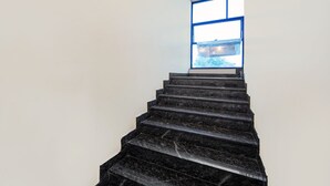 A staircase with black steps leading to a window with blue framing. - Treebo Surya Comforts, 200 Mtrs From Kolhapur Railway Station (Kolhapur)