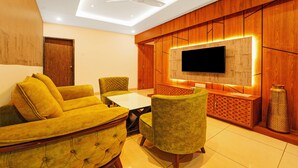 A modern living room with a sofa, chairs, a coffee table, a TV, and wooden paneling. - Treebo Surya Comforts, 200 Mtrs From Kolhapur Railway Station (Kolhapur)