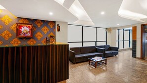 A reception area with a wooden reception desk, a sofa, a coffee table, and a patterned wall. - Treebo Surya Comforts, 200 Mtrs From Kolhapur Railway Station (Kolhapur)