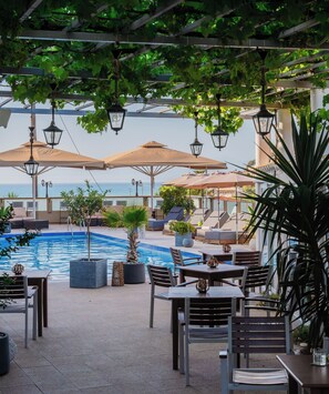 A poolside area with lounge chairs and umbrellas, a pool, and a view of the sea. - Sunsea Wellness Resort (Corfu)