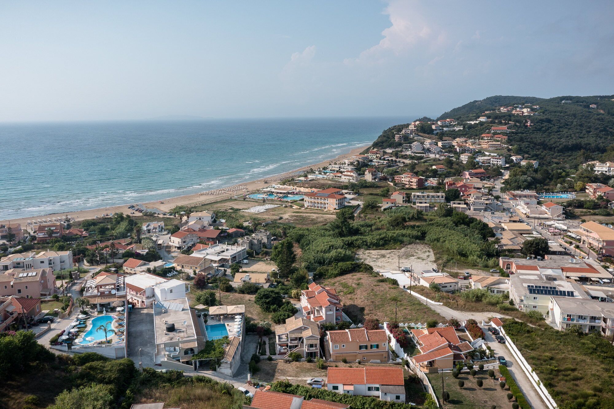 Luftaufnahme einer Küstenstadt mit Strand, Häusern und einem Schwimmbadkomplex.
