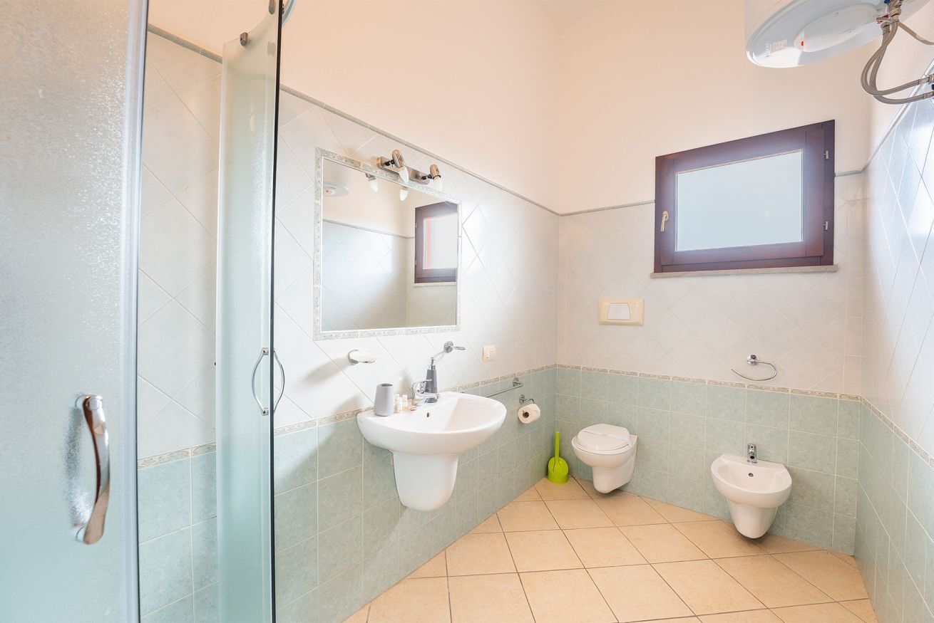 A bathroom with a glass shower enclosure, a sink, a toilet, and a bidet.