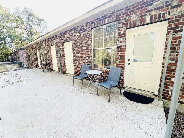 A brick building with a white door, a window, and a small outdoor seating area with two chairs and a table. - Chateau 4, spacious townhouse in Tickfaw, LA (Tickfaw)
