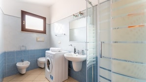 Une salle de bain moderne équipée d’un lave-linge, d’un bidet et d’une douche à parois de verre.