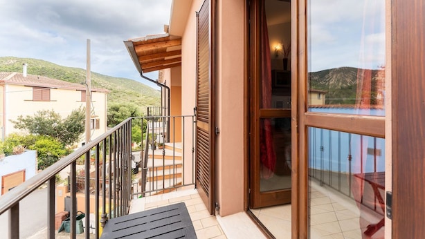 Un balcon agrémenté d’une pergola en bois, d’une porte vitrée et offrant une vue sur une colline.