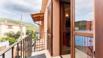 Un balcon agrémenté d’une pergola en bois, d’une porte vitrée et offrant une vue sur une colline.