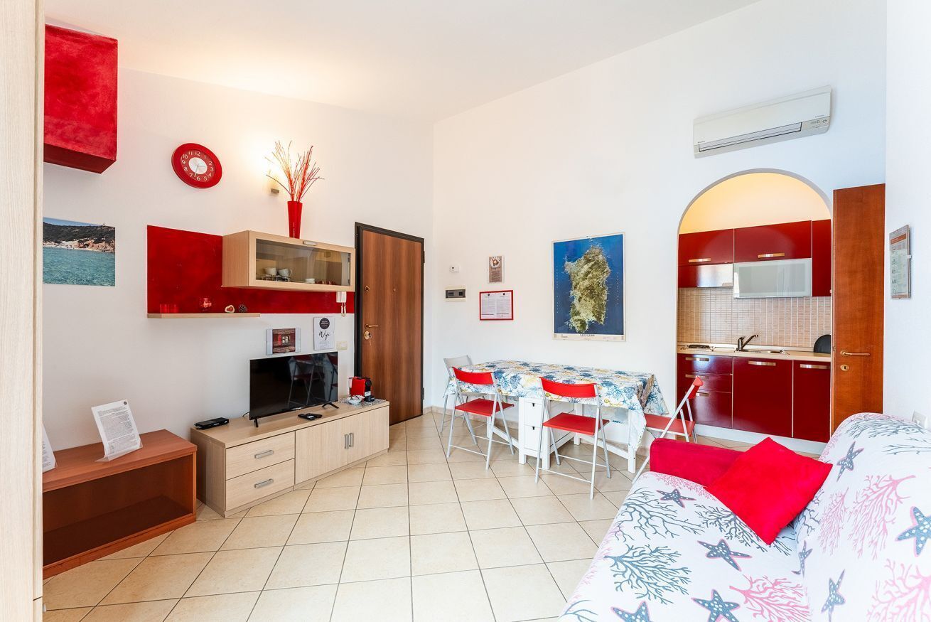 Un espace de vie compact comprenant un coin cuisine, un coin repas et un lit avec un oreiller rouge.