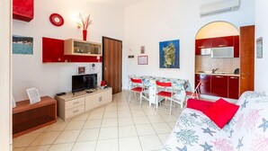 Un espace de vie compact comprenant un coin cuisine, un coin repas et un lit avec un oreiller rouge.
