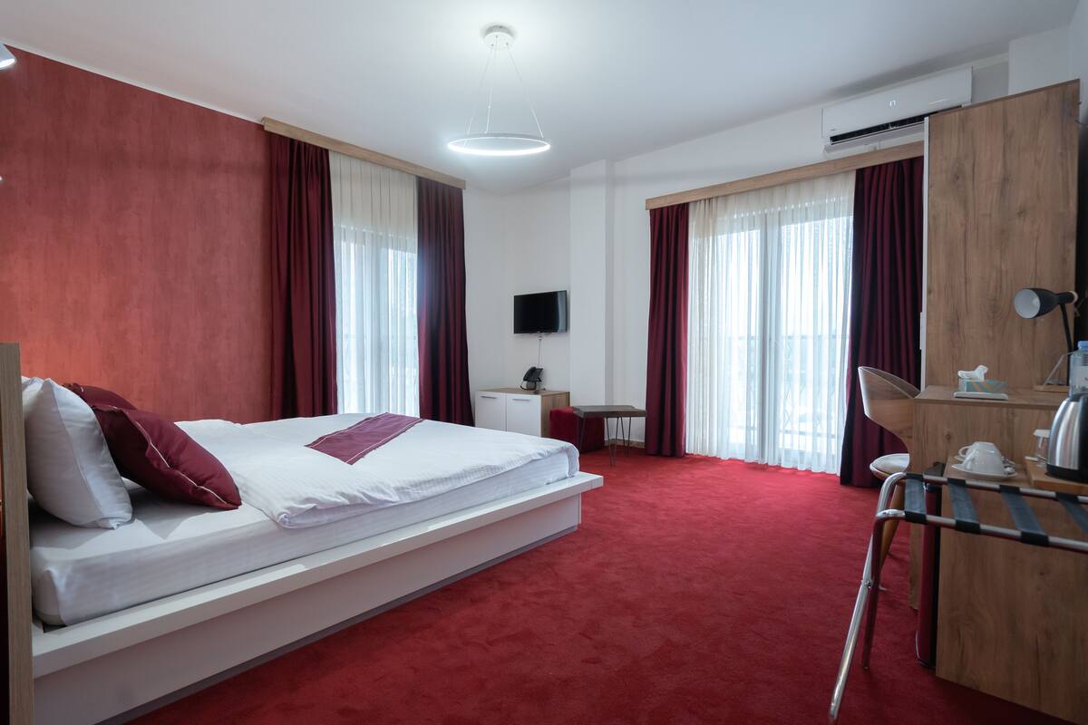 Quarto de hotel com uma cama grande, uma escrivaninha, uma cadeira, uma televisão e um guarda-roupa.